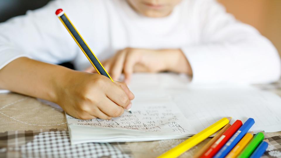 Nahaufnahme eines Kindes, das in ein Heft schreibt. Das Gesicht ist unscharf und nur halb zu erkennen. Nahaufnahme eines Kindes, das in ein Heft schreibt. Das Gesicht ist unscharf und nur halb zu erkennen.