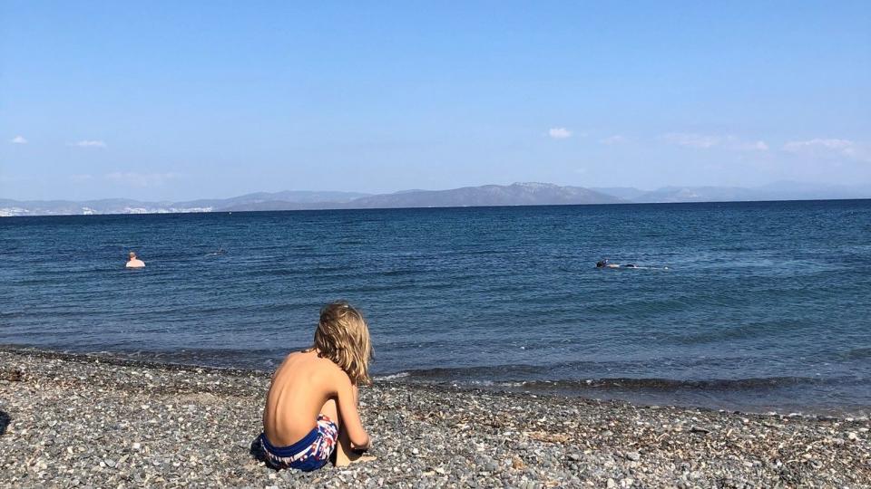 Ein Junge sitzt am Strand und schaut aufs Wasser.