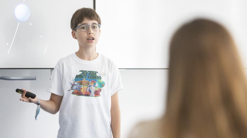 Ein Junge steht vor einem Whiteboard und hält einen Vortrag. Ein Junge steht vor einem Whiteboard und hält einen Vortrag.