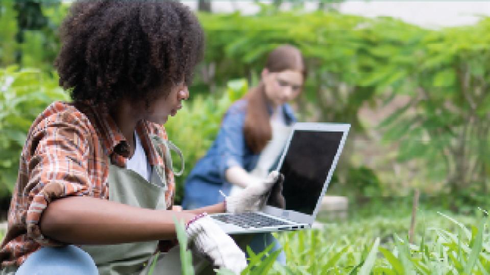 Das Banner zum BundesUmweltWettbewerb zeigt zwei Jugendliche mit Laptop auf einer Wiese.