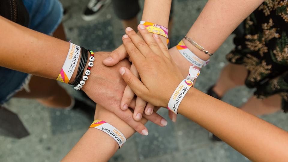 Die Hände von Jugendlichen mit "Demokratisch Handeln"-Armbändchen treffen sich.