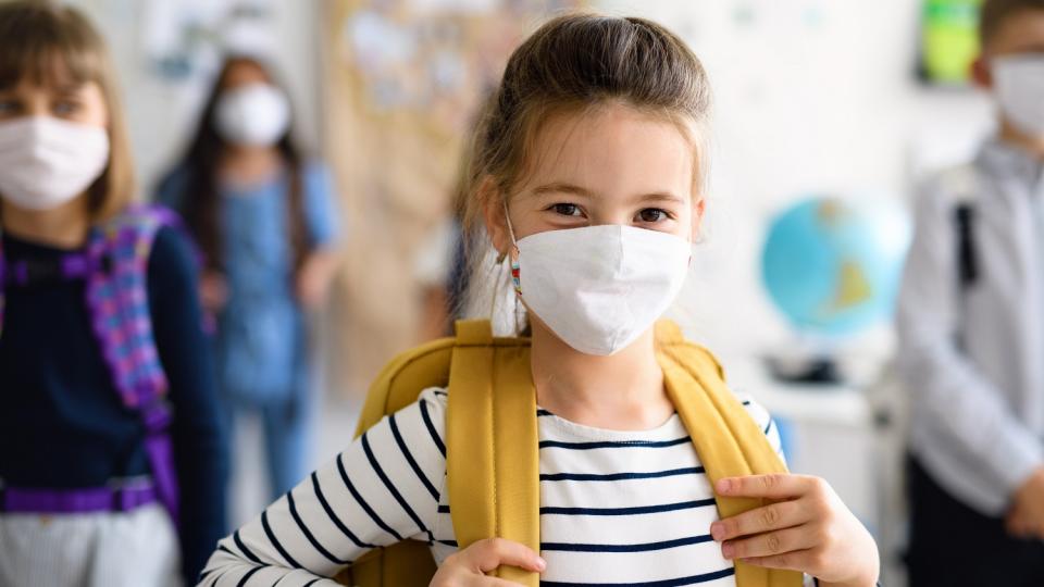 Eine Schülerin mit Maske und Tornister steht in der Schule