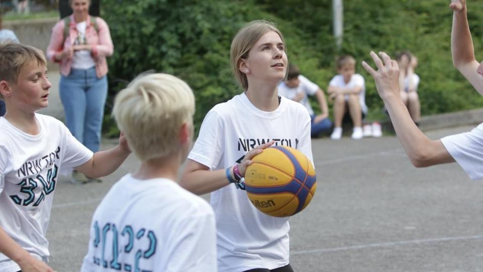 Mädchen und Jungen spielen Streetbasketball.