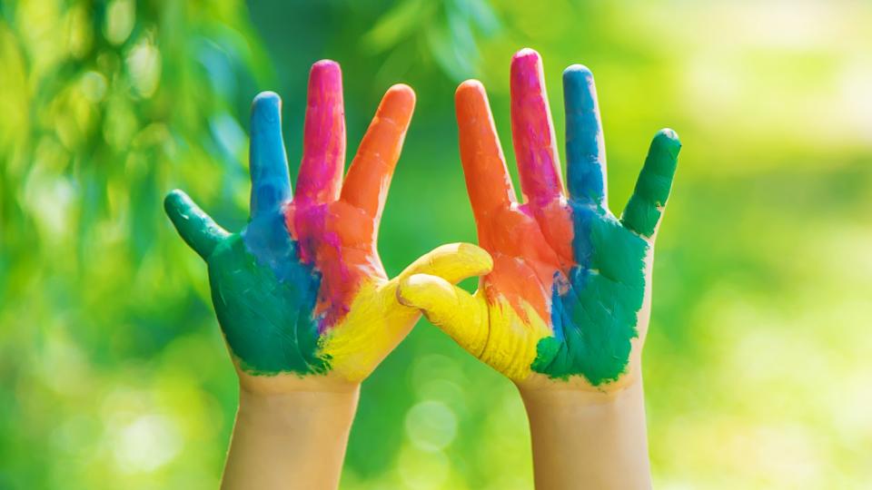 Zwei in Regenbogenfarben bemalte Kinderhände werden hochgehalten. Zwei in Regenbogenfarben bemalte Kinderhände werden hochgehalten.