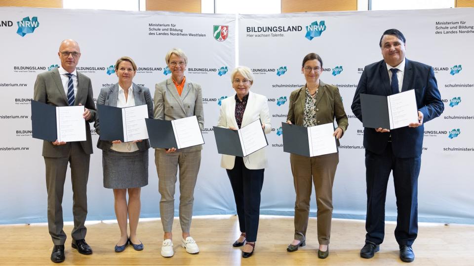 Der Geschäftsführer der Wübben Stiftung Bildung, Dr. Markus Warnke, die Prorektorin Studium der Technischen Universität Dortmund, Prof. Wiebke Möhring (in Vertretung von Rektor der @TU_Dortmund, Prof. Dr. Manfred Bayer), Schulministerin Dorothee Feller, die Vorständin der RAG-Stiftung, Bärbel Bergerhoff-Wodopia, die Rektorin der Universität Duisburg-Essen, Prof. Dr. Barbara Albert und der Rektor der Ruhr-Universität Bochum, Prof. Dr. Dr. h.c. Martin Paul mit Urkunden vor einer "Bildungsland NRW"-Stellwand
