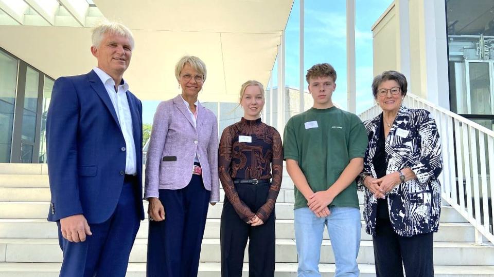 Gruppenbild mit Professor Axel Görlitz, Studiendekan der Mathematisch-Naturwissenschaftlichen Fakultät an der Düsseldorfer Universität, Ministerin, Preisträgerin Hannah Scholten, Preisträger Luis Rosier und Professorin Ingeborg Henzler, Vorstandsmitglied der Dr.-Hans-Riegel-Stiftung, vor einer Treppe zur Dr. Hans Riegel-Fachpreisverleihung 