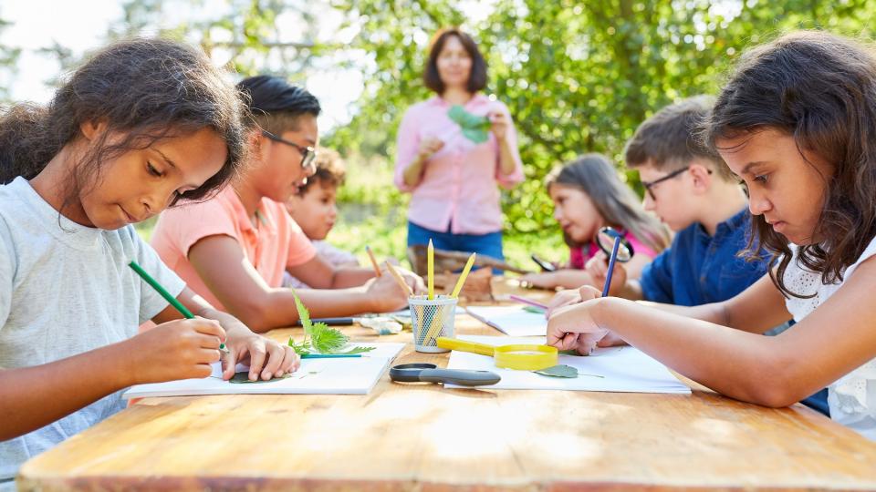 Eine Gruppe von Kindern sitzt draußen an einem Tisch und malt. Eine Gruppe von Kindern sitzt draußen an einem Tisch und malt.