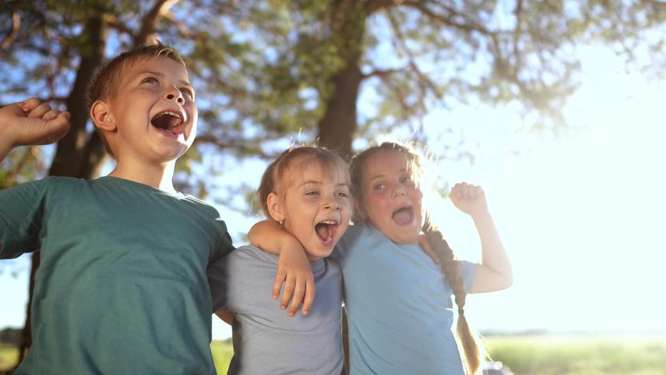 Drei Kinder stehen vor Bäumen und singen laut. Drei Kinder stehen vor Bäumen und singen laut.