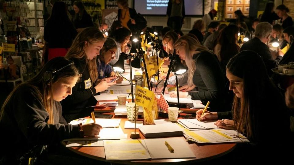 Schülerinnen und Schüler sitzen mit Leselampen an Tischen und schreiben Briefe im Rahmen des Briefmarathons von Amnesty International. Schülerinnen und Schüler sitzen mit Leselampen an Tischen und schreiben Briefe im Rahmen des Briefmarathons von Amnesty International.