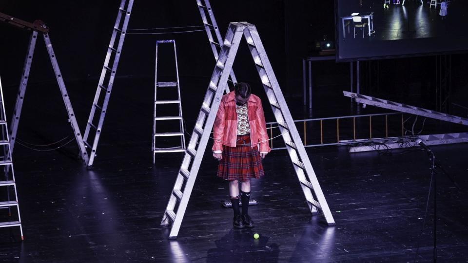 Eine Jugendliche auf der Theaterbühne unter einer Leiter. Eine Jugendliche auf der Theaterbühne unter einer Leiter.