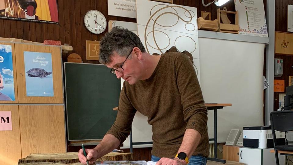 Der Lehrer Gregor Gehling skizziert ein Kunstwerk auf Holz.