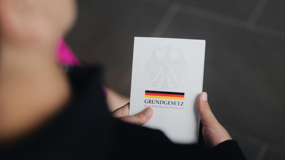 Detailaufnahme einer gedruckten Fassung des Grundgesetzes, das in der Hand eines jungen Menschen liegt. (22. Mai 2024)