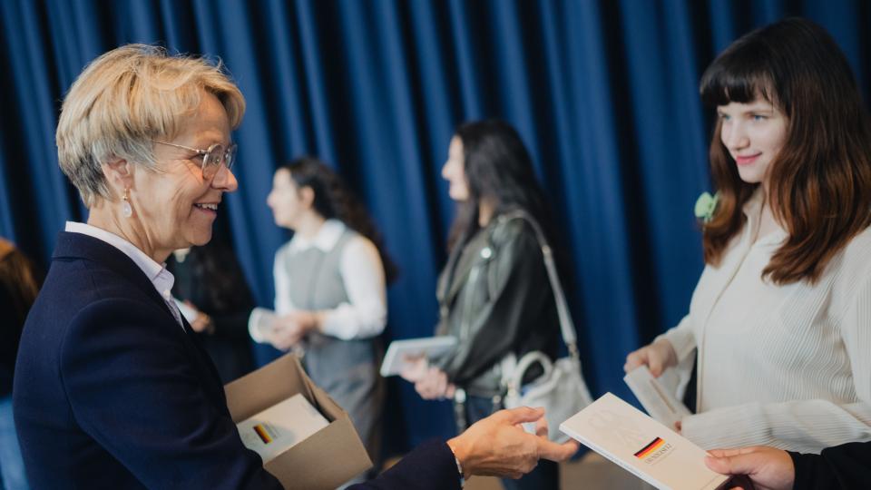 Ministerin Feller teilt Schülerinnen und Schülern der Johannes-Rau-Hauptschule Bonn das Grundgesetz in gedruckter Form aus. (22. Mai 2024)