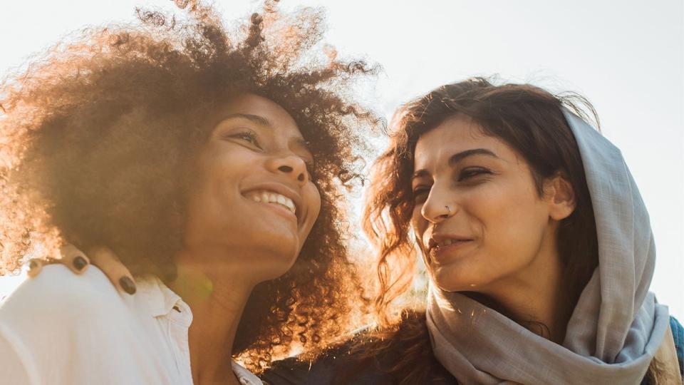 Zwei Frauen mit Migrationshintergrund stehen eng beisammen, eine der beiden trägt ein lockeres Kopftuch. Zwei Frauen mit Migrationshintergrund stehen eng beisammen, eine der beiden trägt ein lockeres Kopftuch.