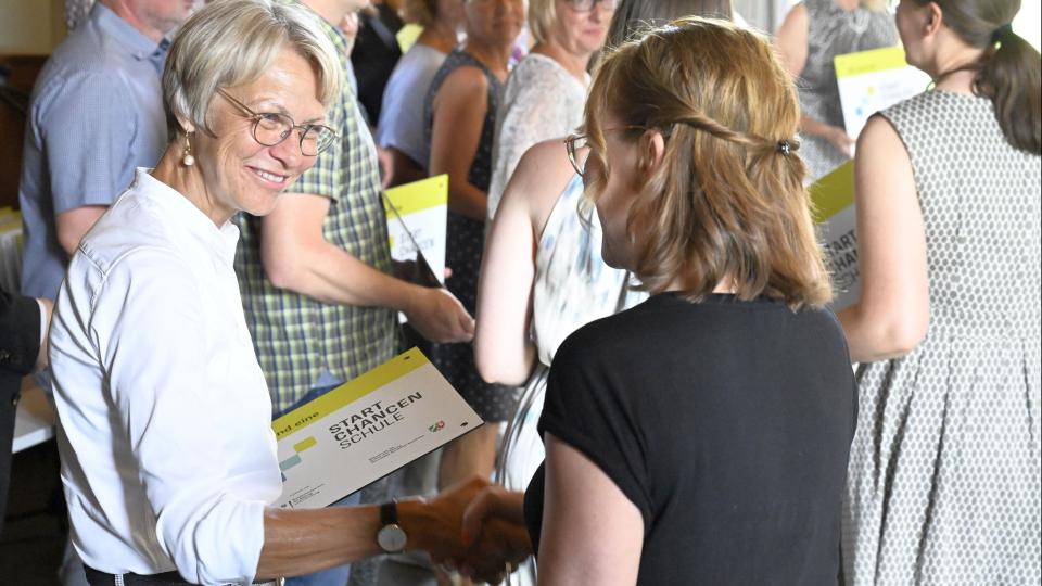 Ministerin Dorothee Feller überreicht einer Schulleiterin eine Startchancen-Plakette. Ministerin Dorothee Feller überreicht einer Schulleiterin eine Startchancen-Plakette.