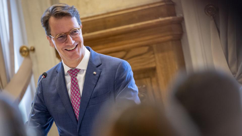 Ministerpräsident Hendrik Wüst spricht vor einer Gruppe Lehramtsreferendarinnen und -referendare, im Hintergrund die Flaggen von Europa, Deutschland und NRW