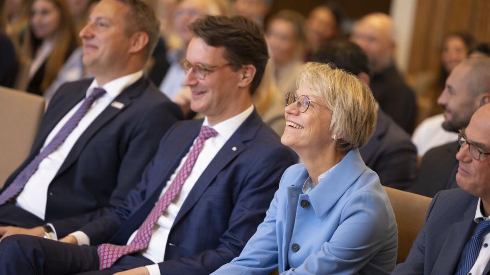 Schulministerin Dorothee Feller, Ministerpräsident Hendrik Wüst und Regierungspräsident Thomas Schürmann lächelnd im Publikum 