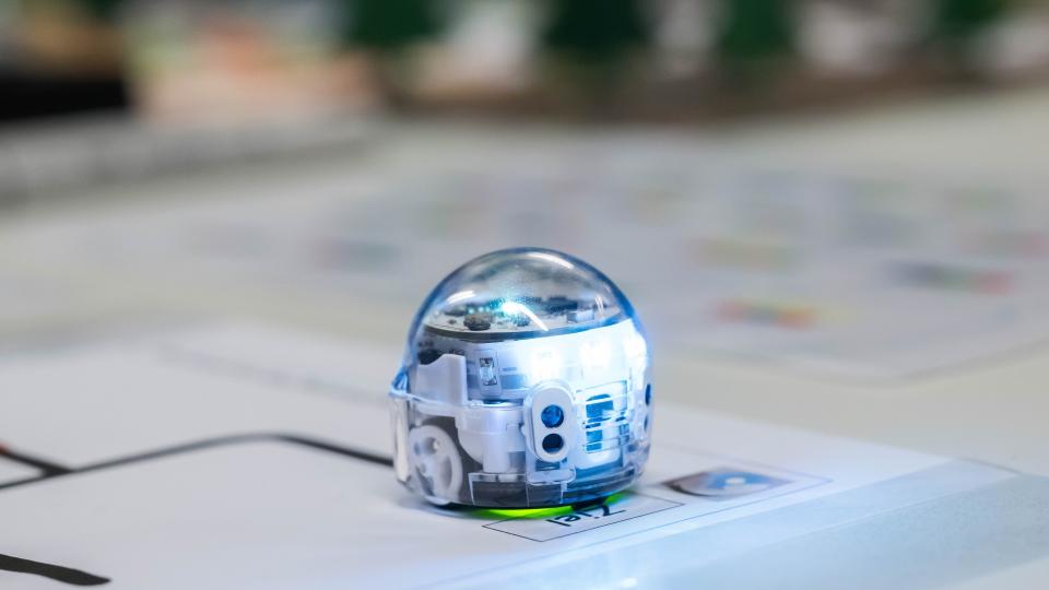 Ein kleiner rundlicher Roboter steht auf einem großen Blatt mit Markierungen auf dem Wort "Ziel". Ein kleiner rundlicher Roboter steht auf einem großen Blatt mit Markierungen auf dem Wort "Ziel".