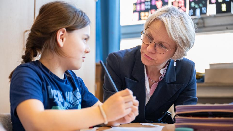 Ministerin Feller sitzt neben einer Schülerin am Tisch.