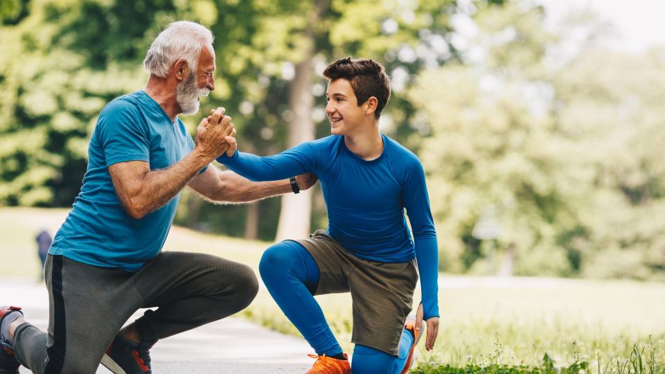 Ein älterer Mann und ein Junge, beide in Sportkleidung, absolvieren gemeinsam Dehnübungen. Ein älterer Mann und ein Junge, beide in Sportkleidung, absolvieren gemeinsam Dehnübungen.