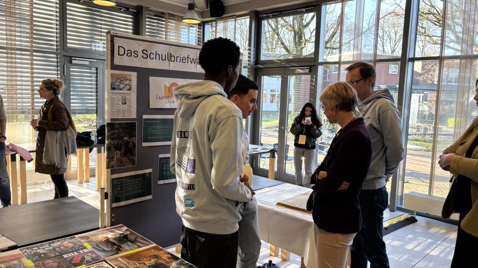Schulministerin Feller steht mit Schülerinnen und Schülern vor einem Stand der Regionalen Lernstatt NRW über die Schulbriefwahl. Schulministerin Feller steht mit Schülerinnen und Schülern vor einem Stand der Regionalen Lernstatt NRW über die Schulbriefwahl.