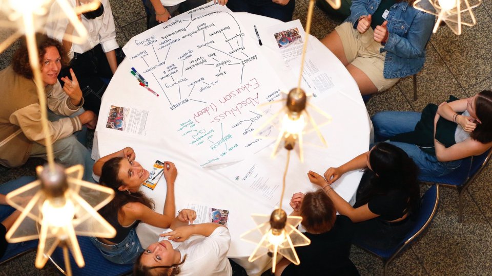 Junge Menschen sitzen gemeinsam um einen Tisch und arbeiten zusammen im Projekt MILeNa. Junge Menschen sitzen gemeinsam um einen Tisch und arbeiten zusammen im Projekt MILeNa.