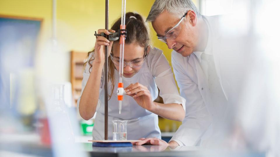 Eine Schülerin experimentiert im Chemieunterricht unter Aufsicht eines Lehrers.