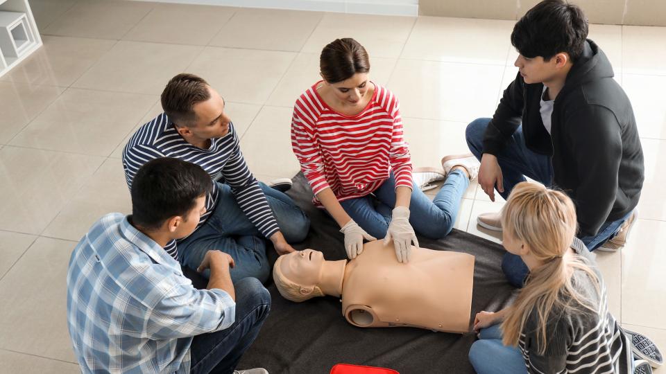 Lehrkräfte, Schülerinnen und Schüler üben die Reanimation an einem Wiederbelebungsphantom.