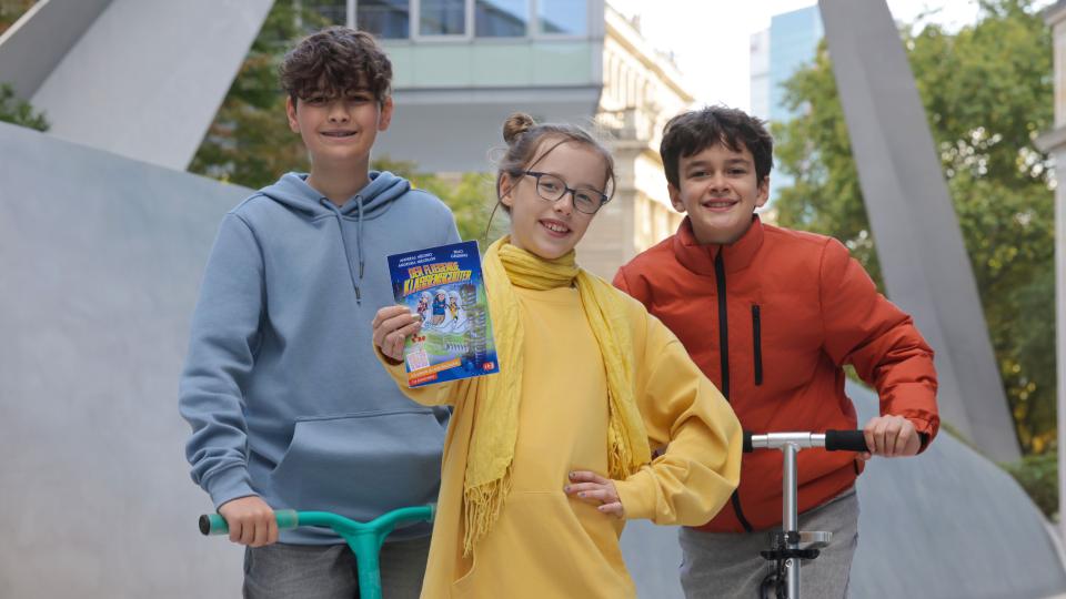 Drei Jugendliche halten das aktuelle Buch der Buch-Gutschein-Aktion 2026 in der Hand.