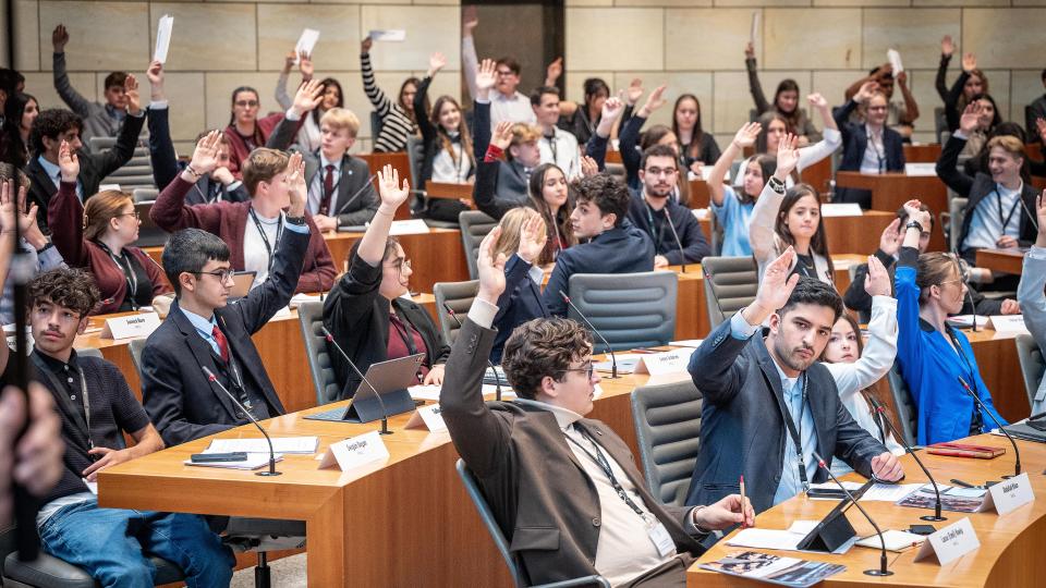 Schülerinnen und Schüler nehmen an einem Aktionstag im Landtag teil und führen eine Abstimmung im Plenarsaal durch.