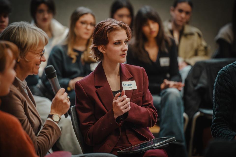 Ministerin Feller mit Handmikrofon umringt von jugendlichen Veranstaltungsteilnehmenden