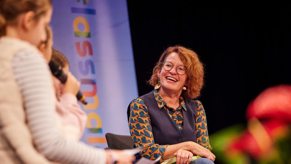 Bei einer Lesung sitzen Schülerinnen mit auf dem Podium und stellen Fragen.
