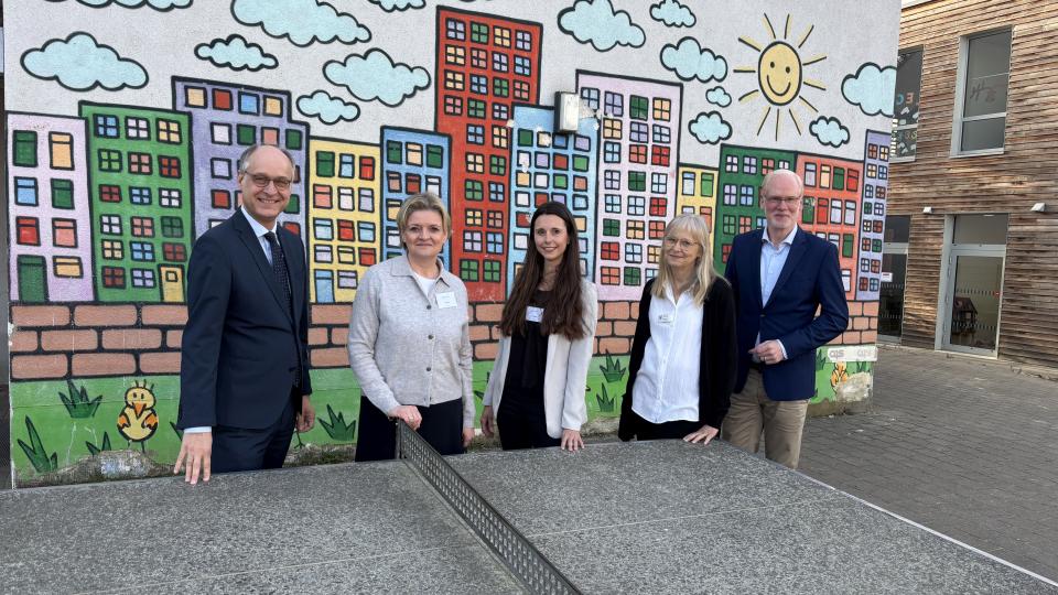 An der Südparkschule Gladbeck stehen Sts Dr. Mauer, Schulleiterin Viola Beyer, Laura Theben (erweiterte Schulleitung, Klassenlehrerin), Natascha Stahl von der Schulaufsicht Recklinghausen, Martin Teuber, Referatsleiter 33 im MSB an einer Tischtennisplatte.