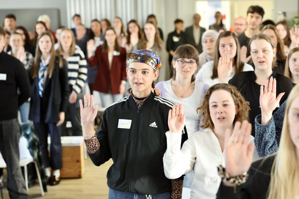 Junge Frauen und Männer stehen in einer Gruppe und haben die Hand zum Eid erhoben.