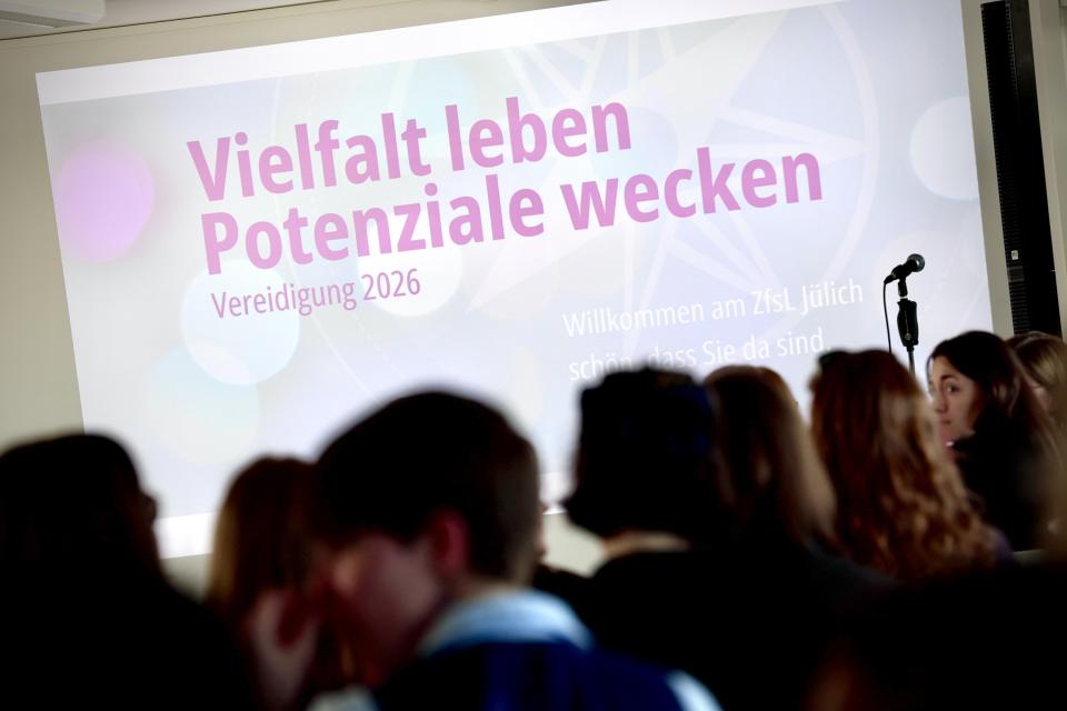 Beamerprojektion mit dem Schriftzug "Vielfalt leben - Potenziale wecken" Vereidigung 2026, davor die Umrisse einer Menschengruppe.