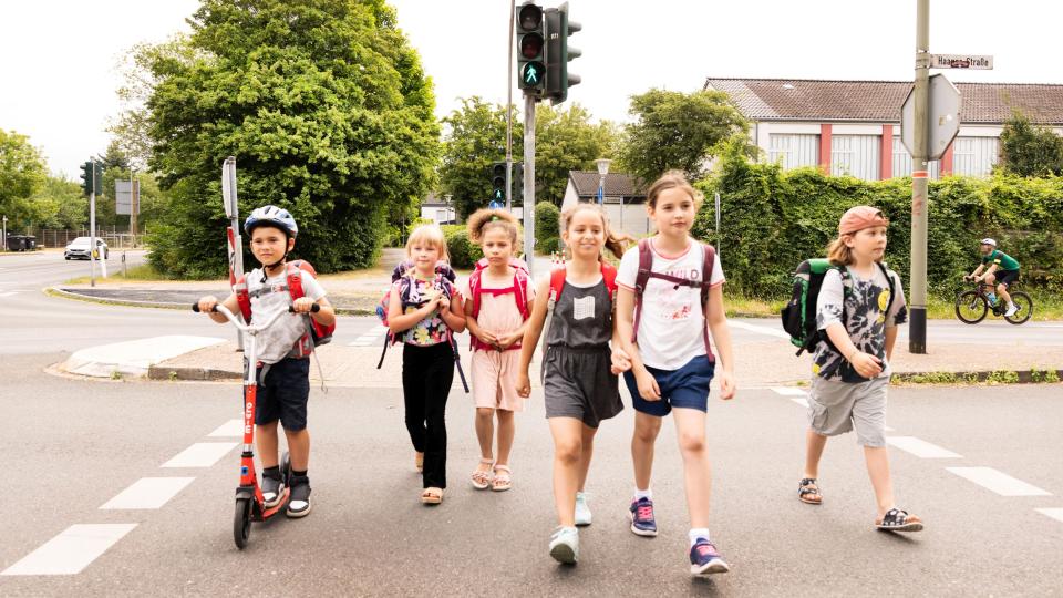 Eine Gruppe Kinder mit Tornistern überquert eine Straße.