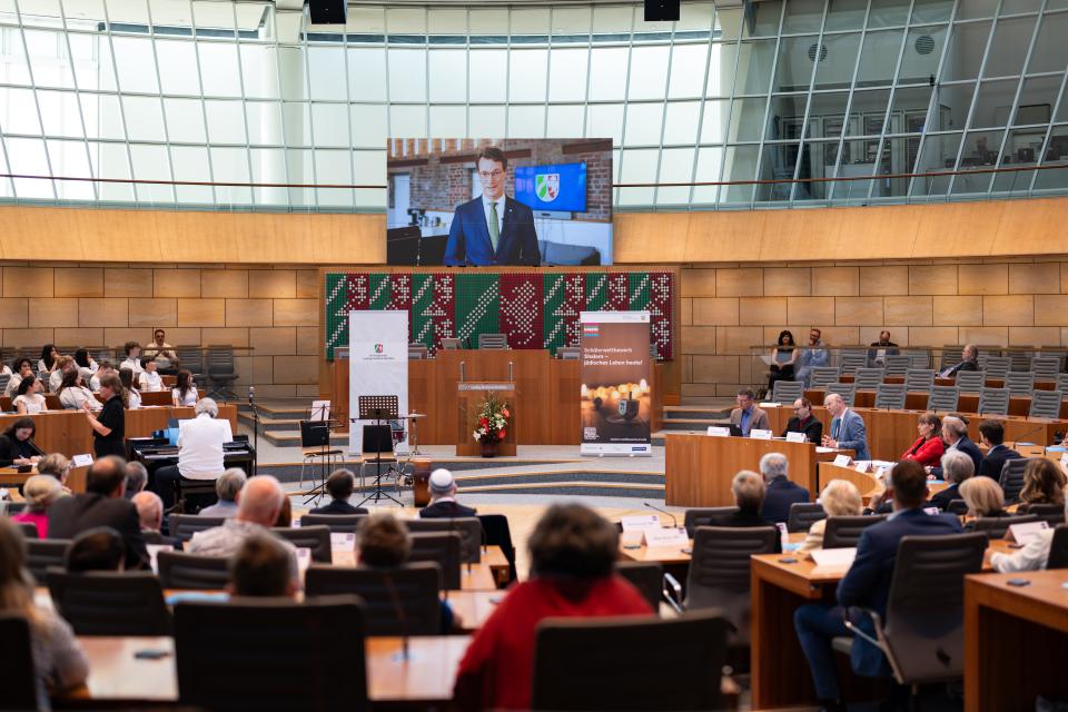 Im Landtag wird über eine Videoleinwand ein Grußwort von Ministerpräsident Hendrik Wüst übertragen.