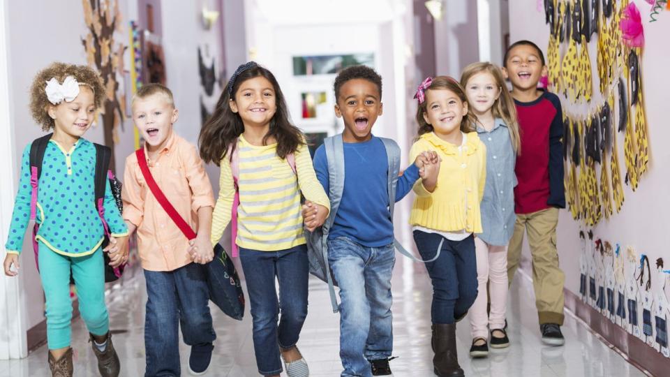 Vorschulkinder laufen Hand in Hand durch einen Schulflur.