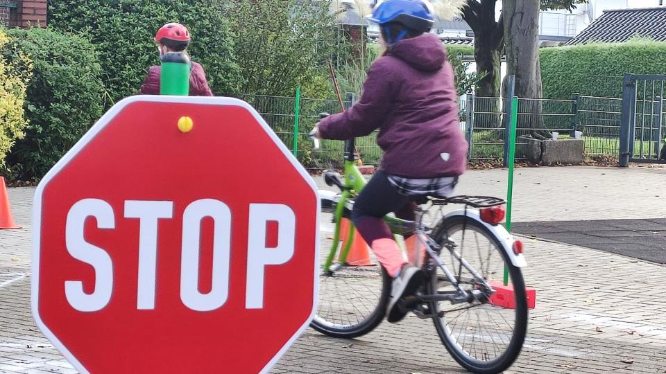 Ein Kind fährt Fahrrad, im Vordergrund steht ein Stop-Schild