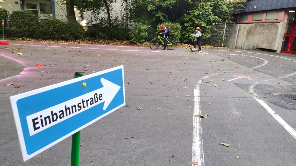 Kinder auf Fahrrädern, im Vordergrund ein Einbahnstraßen-Schild