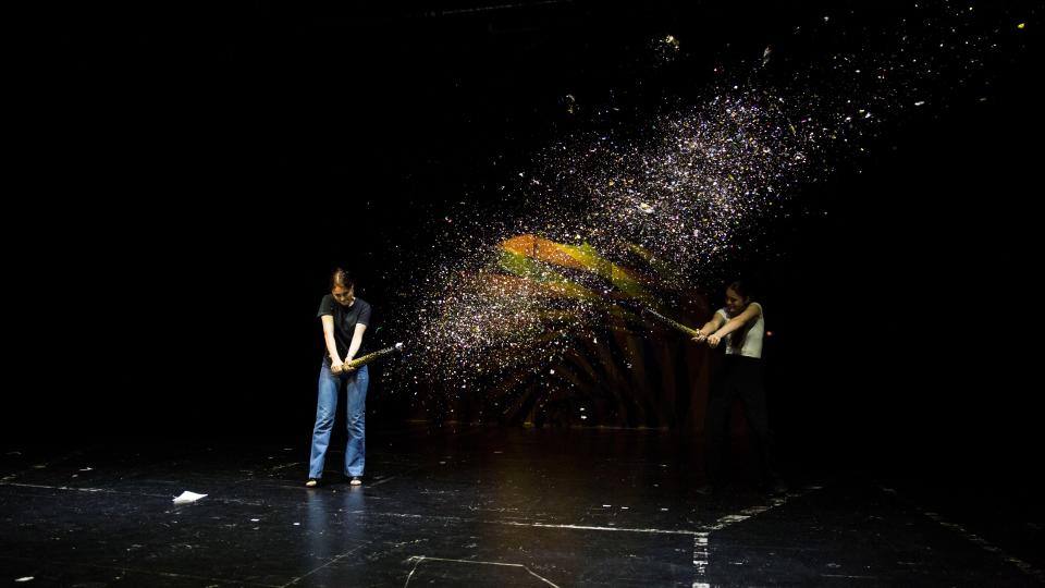 Zwei junge Frauen starten Konfettikanonen auf einer großen Theaterbühne.