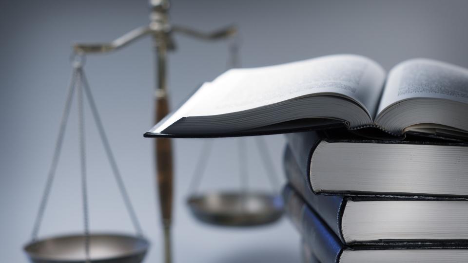 Symbolbild Recht: Im Vordergrund ein Stapel Bücher, im Hintergrund eine Waage. Symbolbild Recht: Im Vordergrund ein Stapel Bücher, im Hintergrund eine Waage.