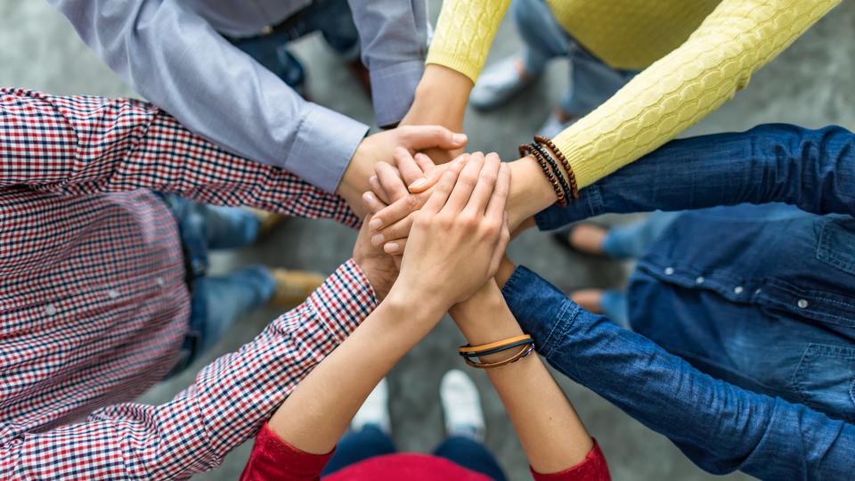 Fünf Menschen stehen im Kreis und legen ihre Hände aufeinander, die Gesichter sind nicht zu erkennen.