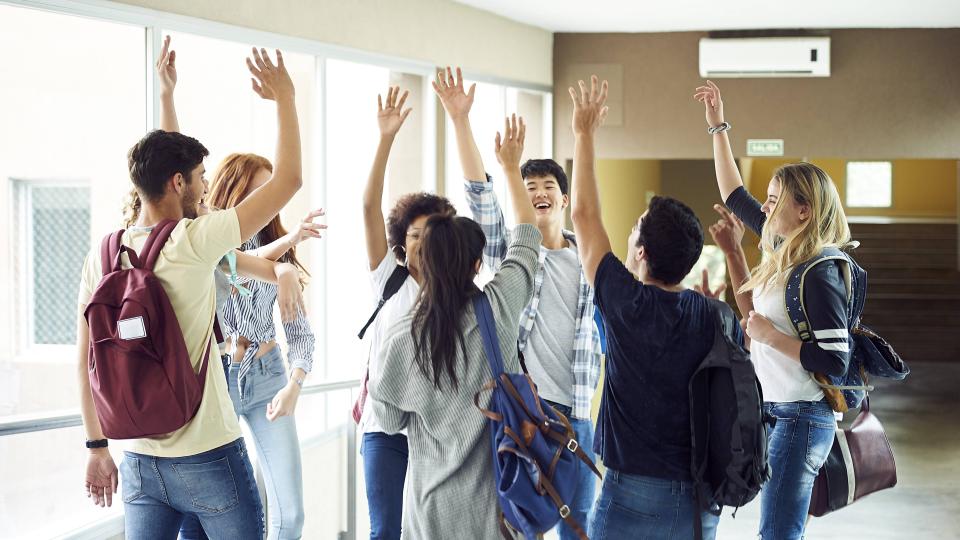 Eine Gruppe Schüler steht in einem Schulflur und hat die Hände zum "High Five" erhoben. Eine Gruppe Schüler steht in einem Schulflur und hat die Hände zum "High Five" erhoben.
