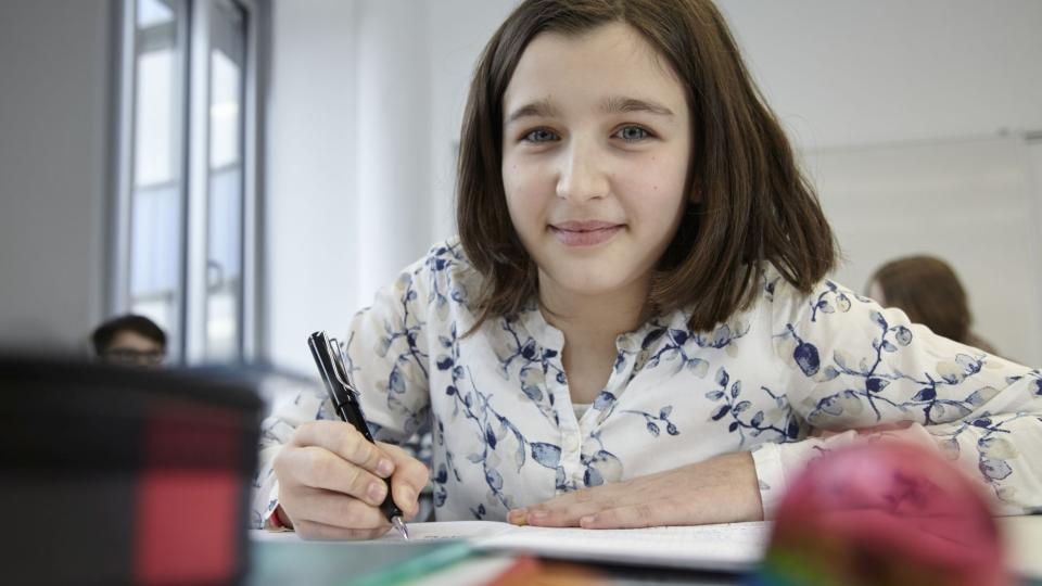 Schülerin sitzt im Unterricht an einem Tisch und schreibt. Schülerin sitzt im Unterricht an einem Tisch und schreibt.