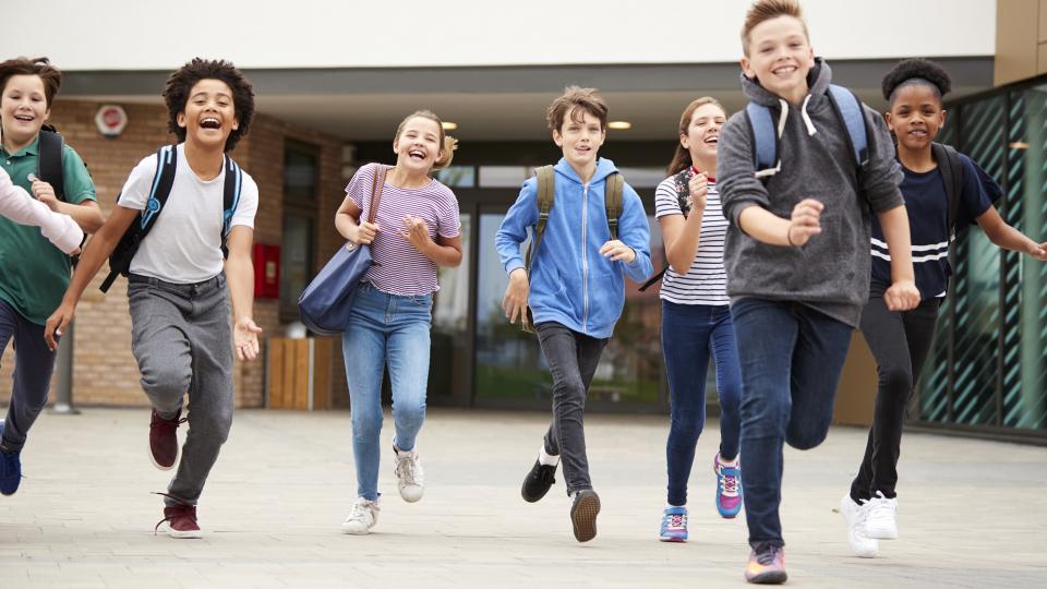 Gruppe von Schülerinnen und Schülern verlässt fröhlich rennend ein Schulgebäude.