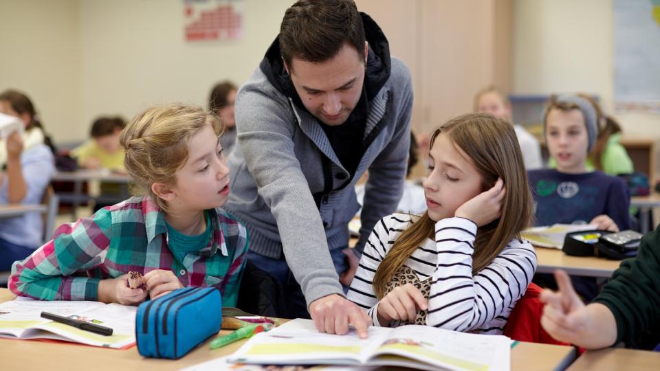 Ein Lehrer mit Migrationshintergrund in einer Unterrichtssituation mit zwei Schülerinnen.