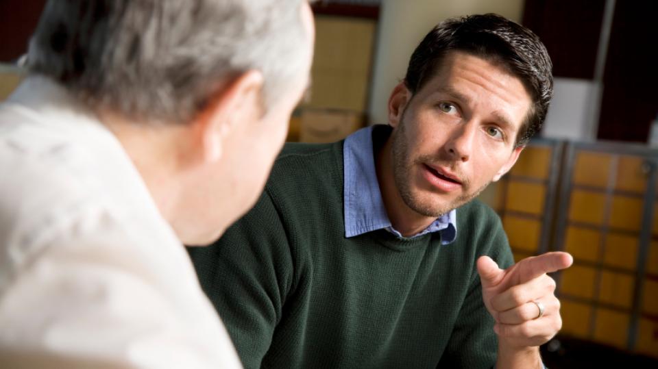 Zwei Männer sprechen miteinander, Blick über die Schulter des einen auf das Gesicht des anderen. Zwei Männer sprechen miteinander, Blick über die Schulter des einen auf das Gesicht des anderen.