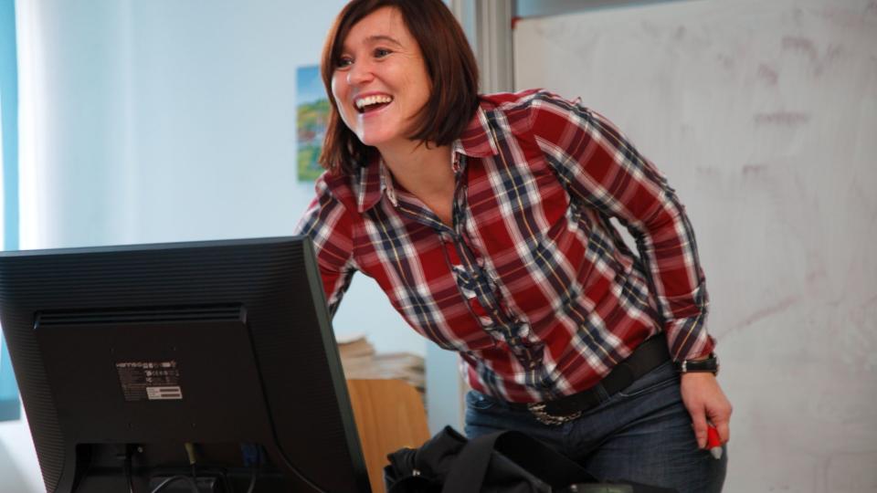 Lehrerin beugt sich lachend zu einem Computerbildschirm.
