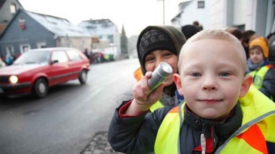 Grundschüler mit Warnweste und Taschenlampe im Straßenverkehr.